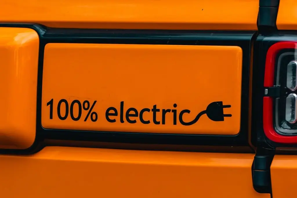 Vibrant orange electric vehicle with a 100% electric emblem, showcasing eco-friendly transportation.